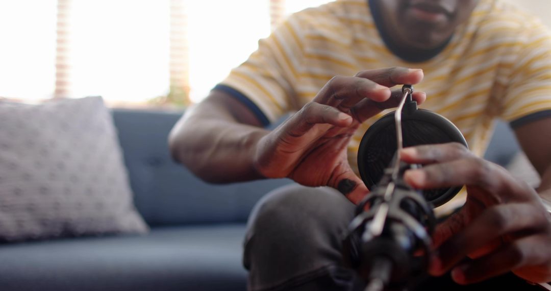 Leaning forward man adjusting microphone and headphones on cozy home studio couch