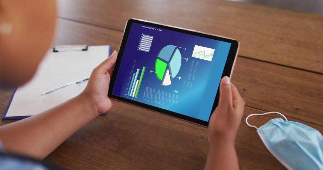Person Viewing Business Statistics on Tablet Display at Wooden Desk