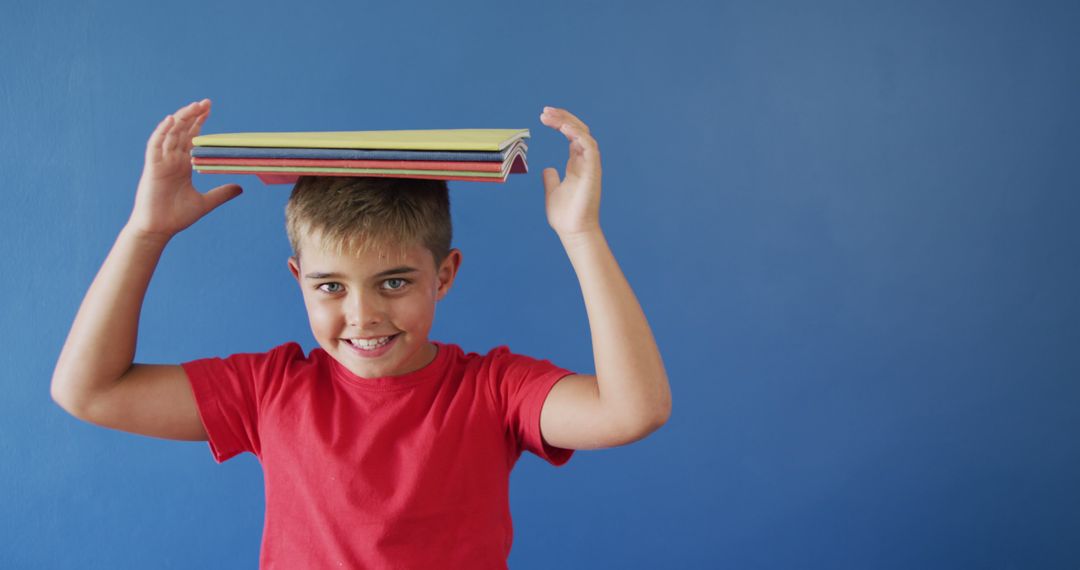 Boy Balancing Books on Head Against Blue Wall - Free Images, Stock Photos and Pictures on Pikwizard.com