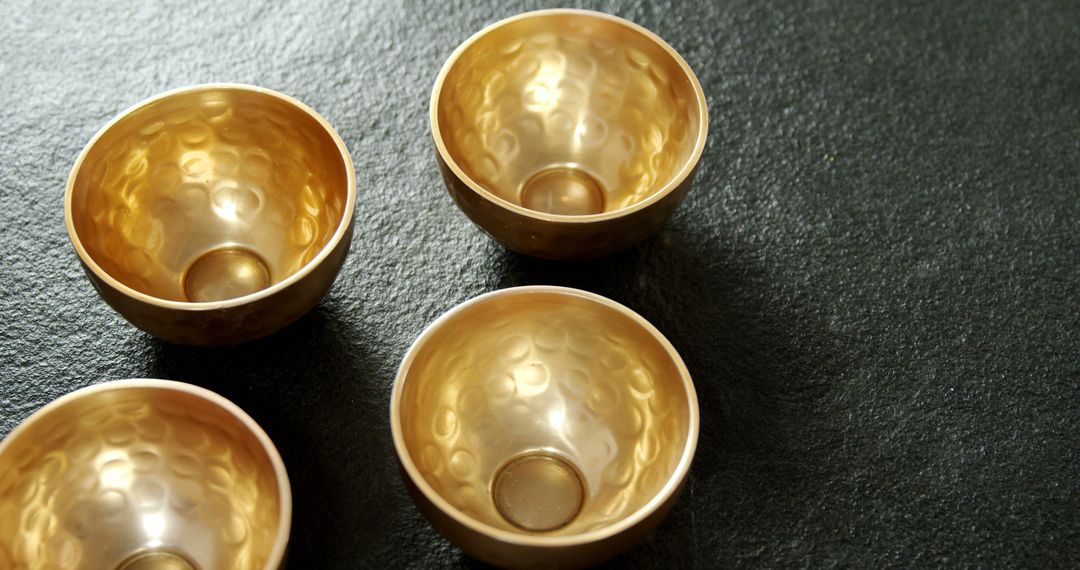 Golden hammered metal bowls on dark textured surface - Free Images, Stock Photos and Pictures on Pikwizard.com