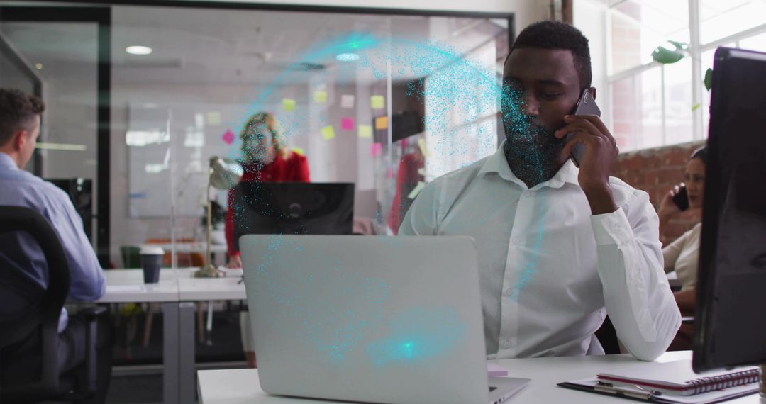 Businessman talking on phone while working on laptop and collaborating in modern open-plan office