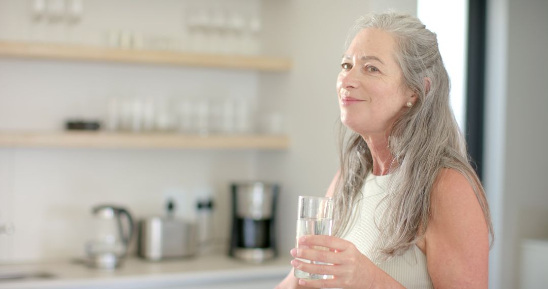 Mature Woman Enjoying Refreshing Glass of Water in Modern Kitchen