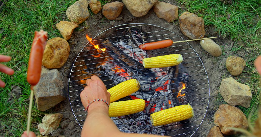 High angle view of friends roasting hot dog and corn on campfire - Free Images, Stock Photos and Pictures on Pikwizard.com