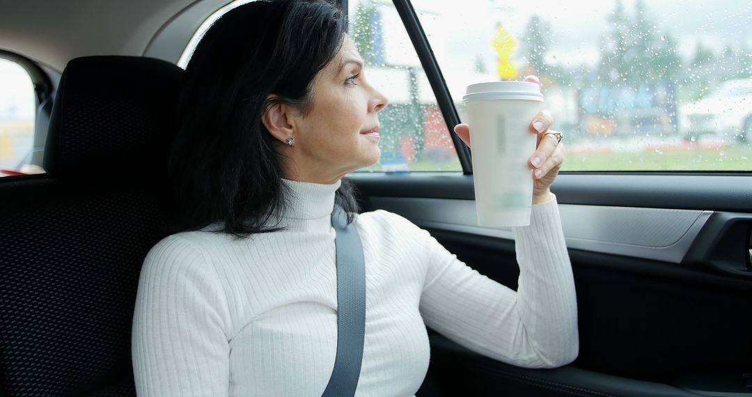 Mature Woman in White Sweater Drinking Coffee in Car on Rainy Day - Free Images, Stock Photos and Pictures on Pikwizard.com