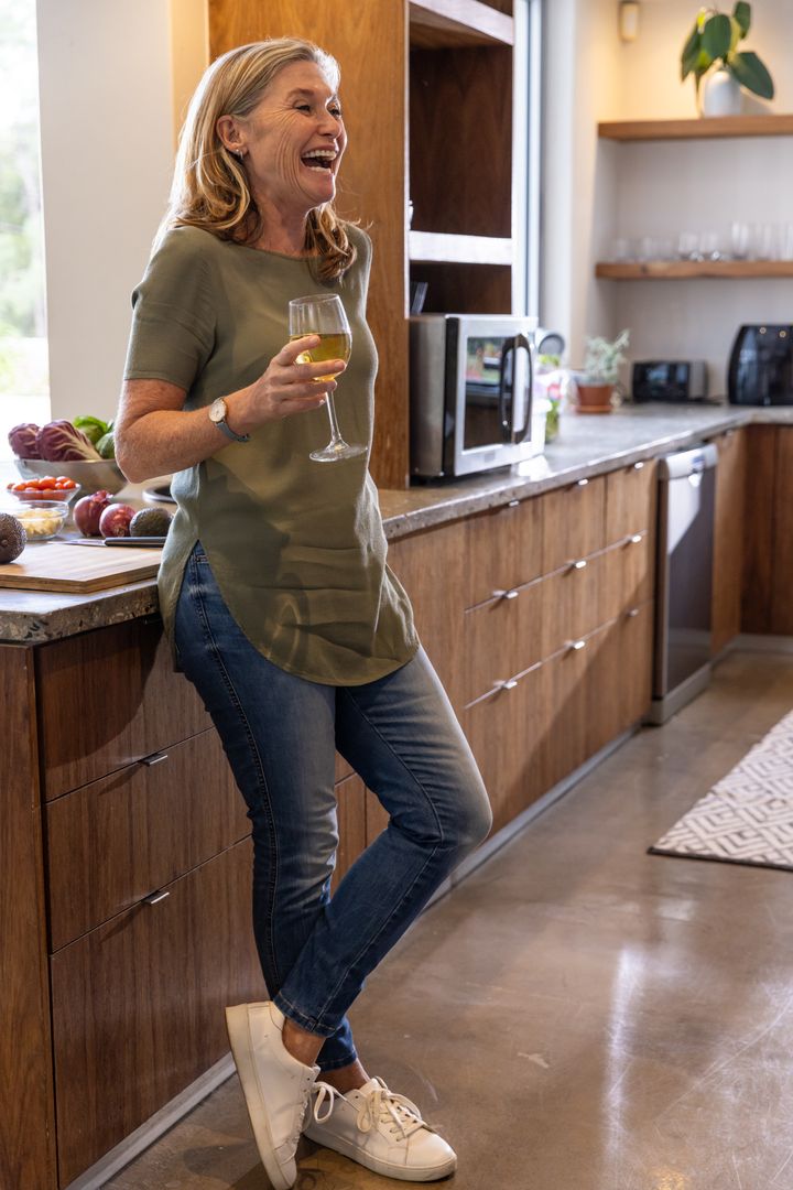 Middle-aged Woman Enjoying Wine and Laughter in Modern Kitchen