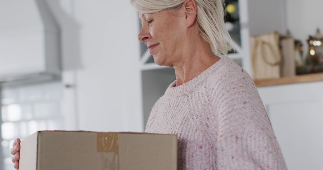 Senior Woman Carrying Cardboard Box in Kitchen - Free Images, Stock Photos and Pictures on Pikwizard.com