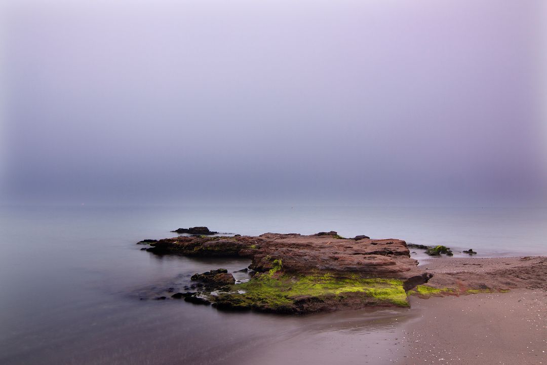 Serene Rocky Beach with Calm Misty Water and Purple Sky - Free Images, Stock Photos and Pictures on Pikwizard.com