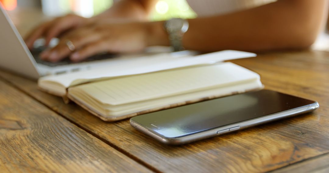 Close-up of smartphone, notepad, and person using laptop on wooden desk - Free Images, Stock Photos and Pictures on Pikwizard.com