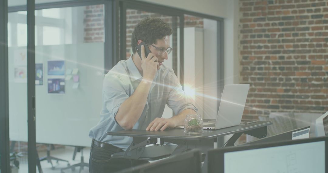 Businessman Engaging in Phone Call at Standing Desk with Laptop