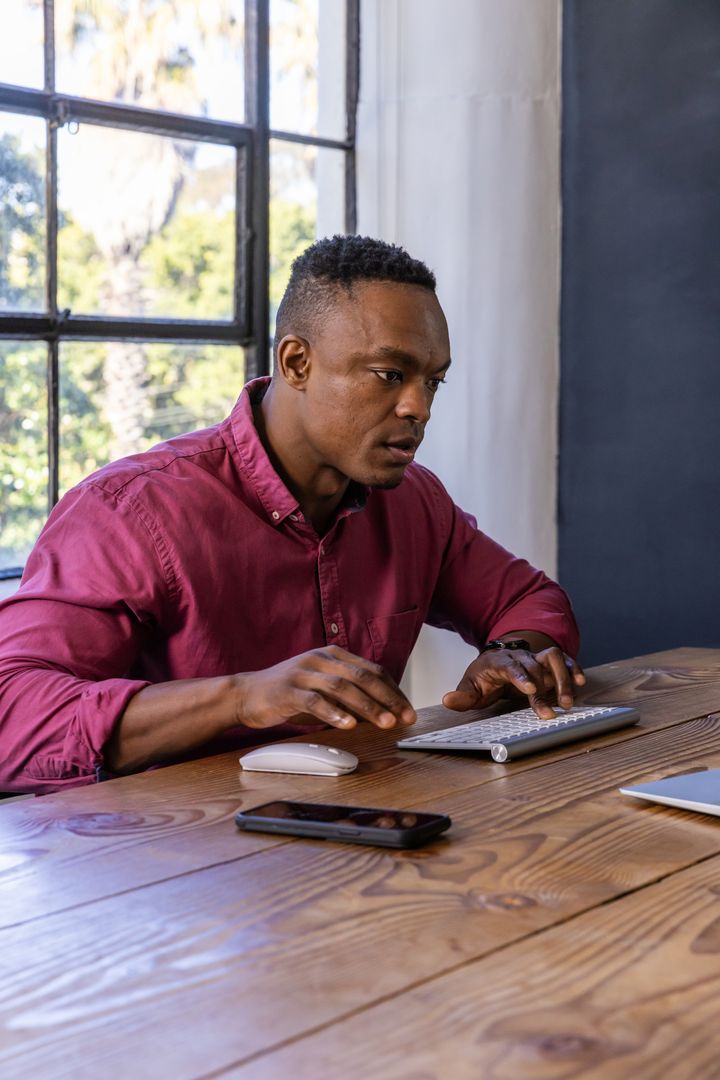 Young Professional Using Computer and Smartphone at Deskside Workspace