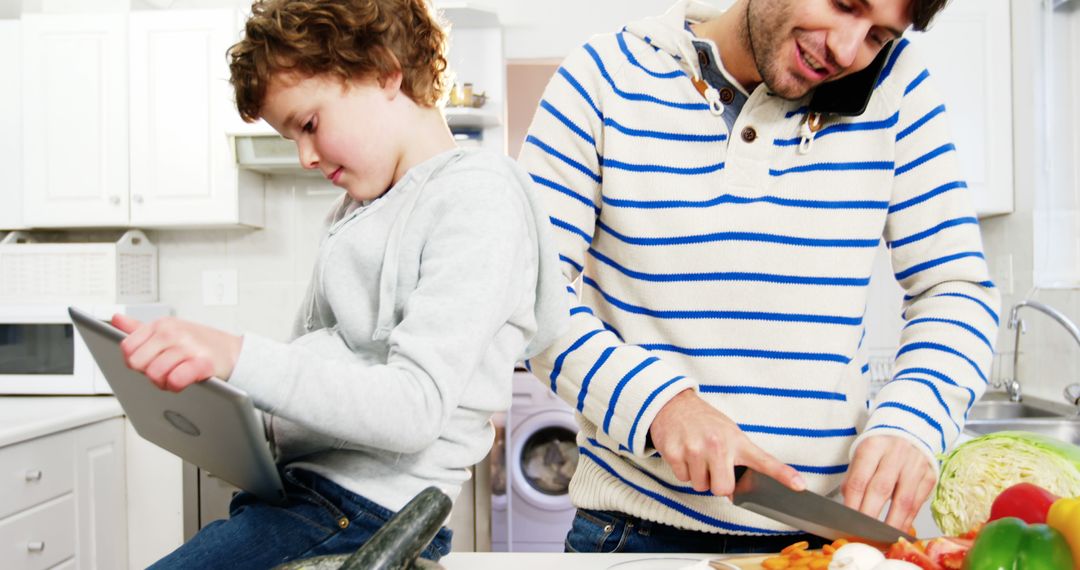 Father Preparing Meal While Son Uses Tablet in Modern Kitchen - Free Images, Stock Photos and Pictures on Pikwizard.com