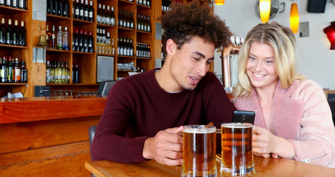 Joyful Friends Enjoying Drinks While Sharing Smartphone at Bar