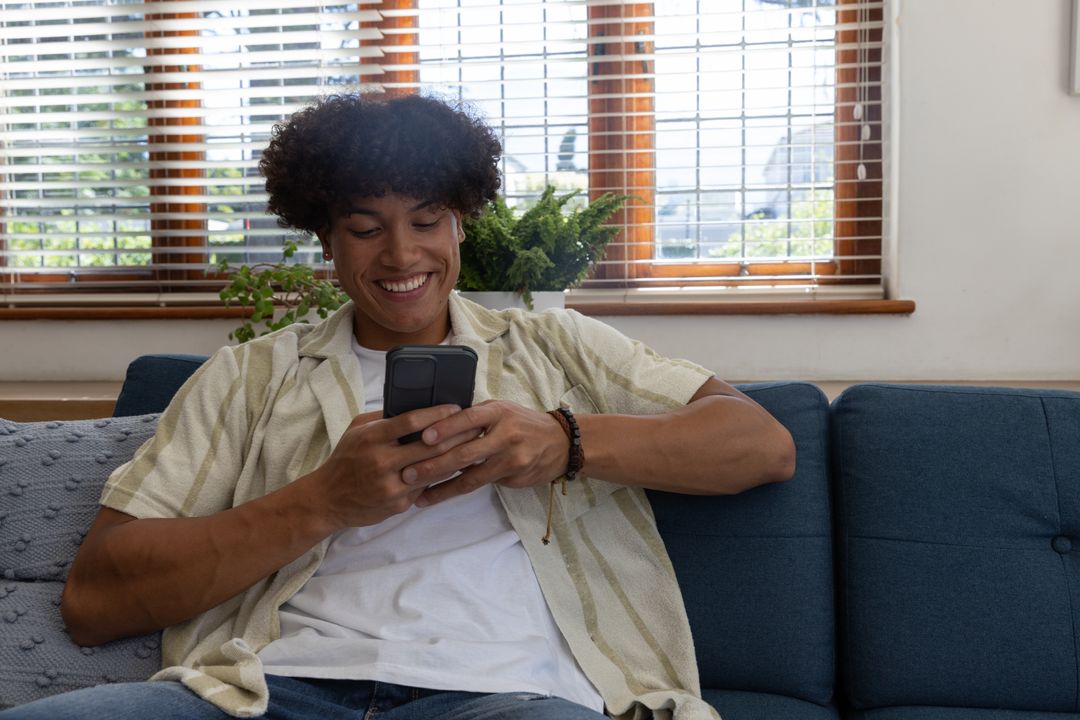 Young Man Relaxing with Smartphone on Cozy Blue Sofa at Home