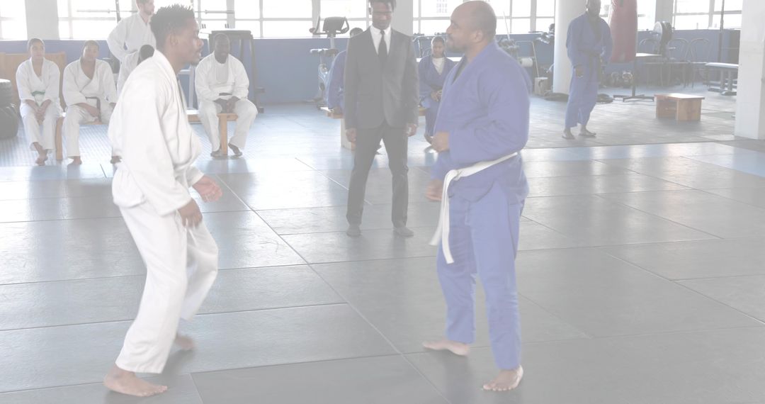 Sparring martial artists wearing white and blue gis on dojo mats practicing combat training