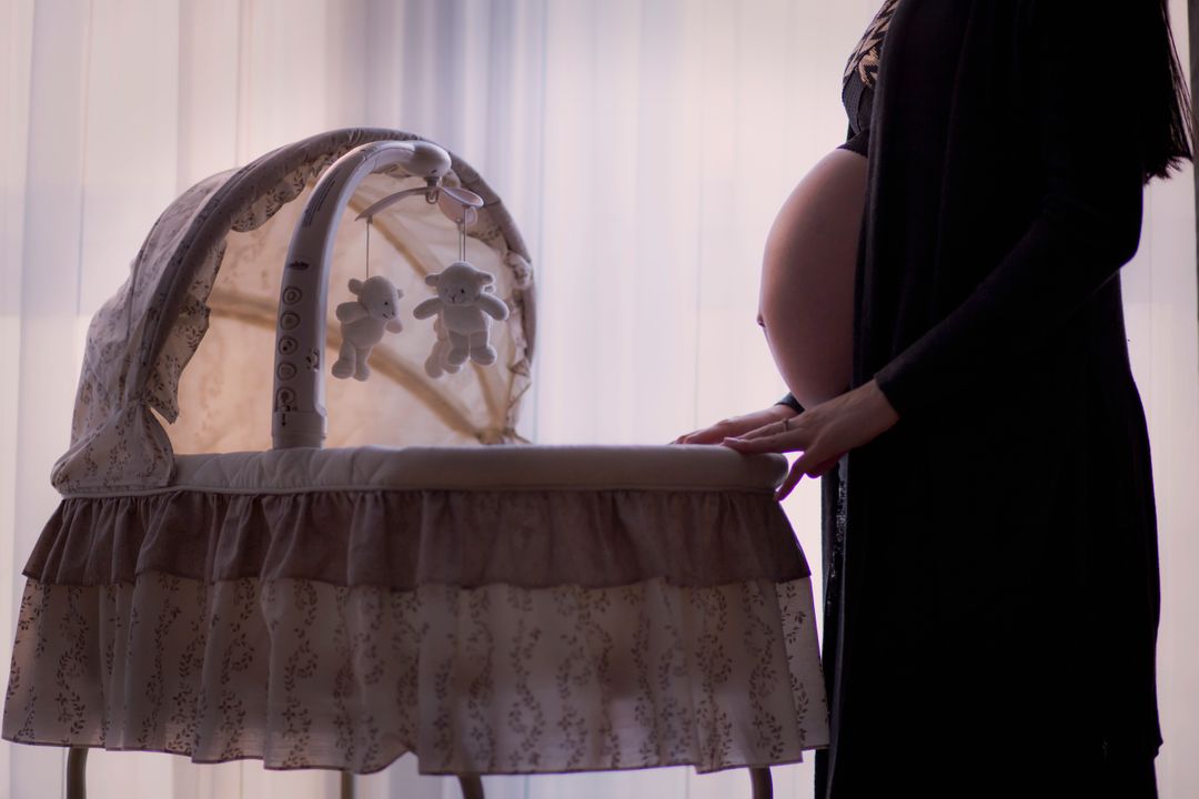 Pregnant Woman Standing by Baby Bassinet in Soft Lighting - Free Images, Stock Photos and Pictures on Pikwizard.com