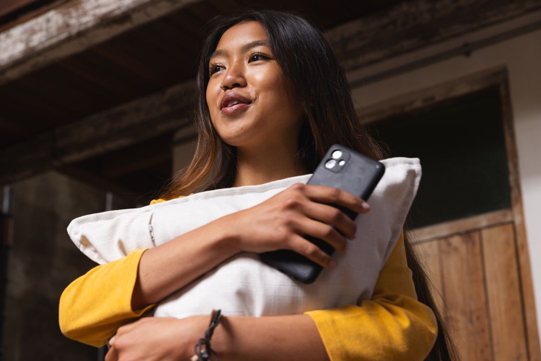Asian Woman Relaxing in Rustic Cabin with Pillow and Smartphone
