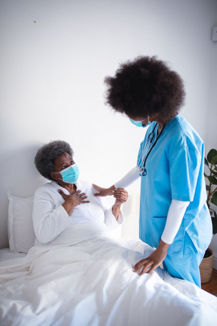 African american female doctor wearing face mask treating senior woman at home - Free Images, Stock Photos and Pictures on Pikwizard.com