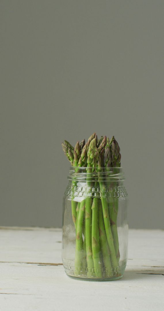 Fresh Asparagus in Glass Jar on Neutral Background