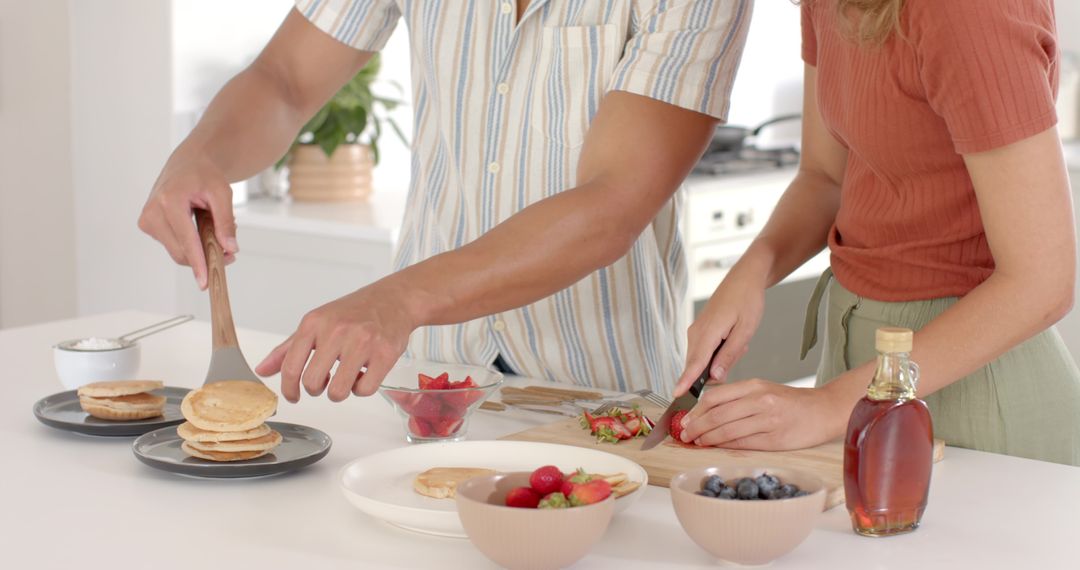 Diverse Couple Preparing Pancakes and Fruits in Modern Kitchen Setting