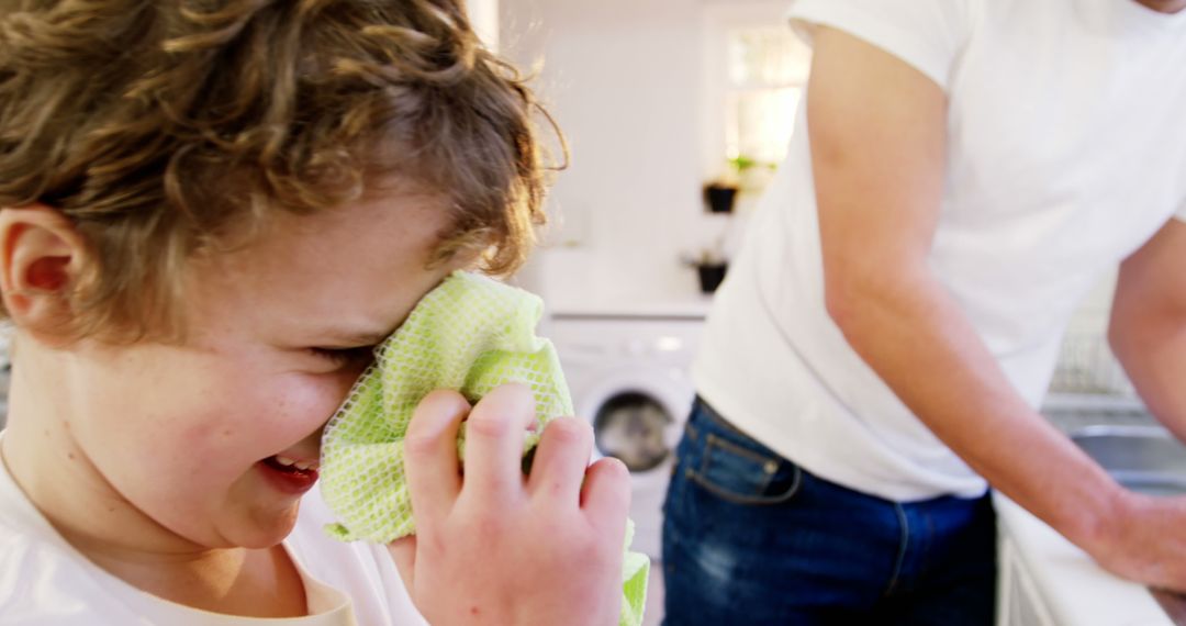 Young Boy Wiping Face in Kitchen with Parent in Background - Free Images, Stock Photos and Pictures on Pikwizard.com