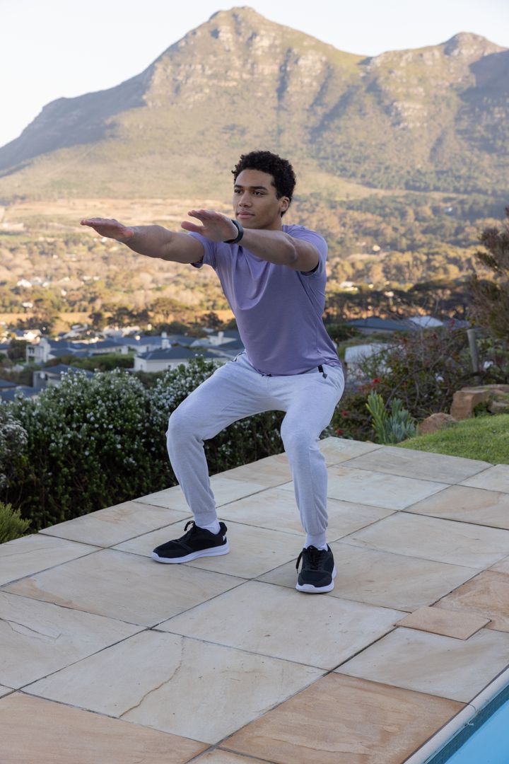 Man Performing Squat on Patio with Mountain Backdrop