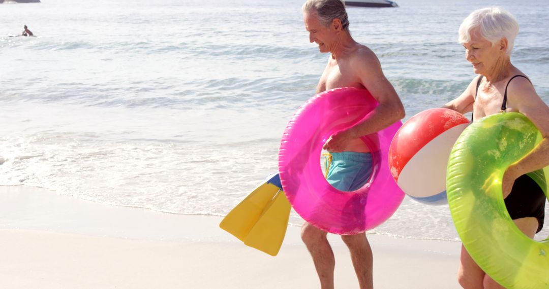 Elderly Couple Enjoying Beach with Inflatable Toys - Free Images, Stock Photos and Pictures on Pikwizard.com