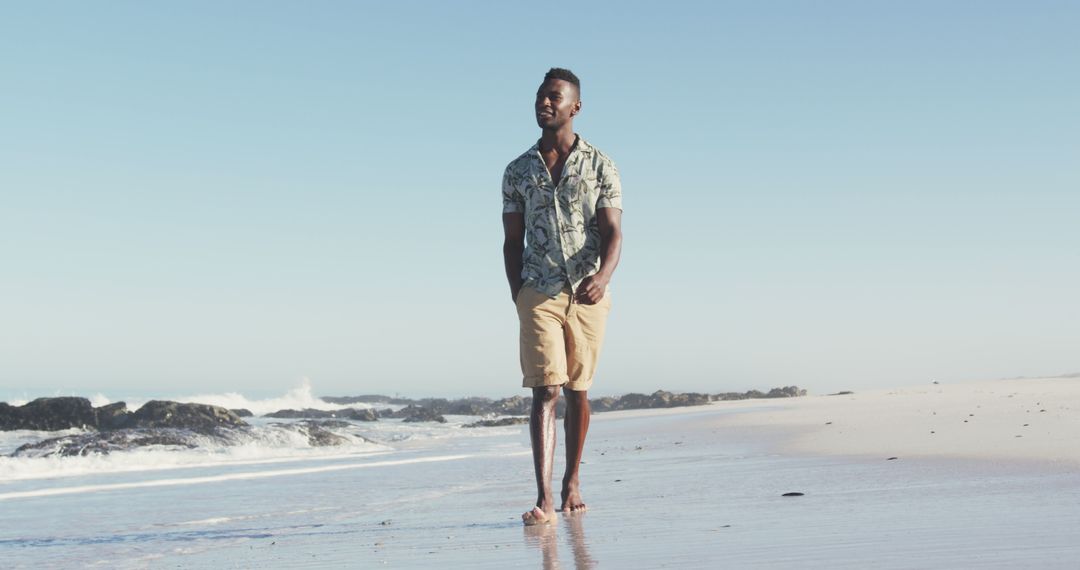 Happy african american man walking barefoot on sunny beach by the sea - Free Images, Stock Photos and Pictures on Pikwizard.com