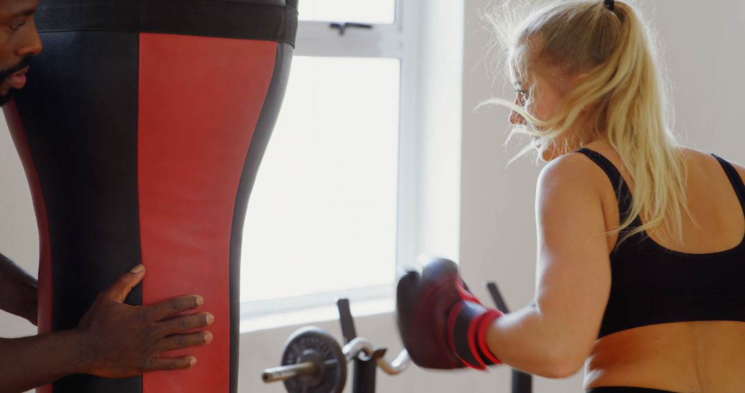 A determined young woman intensely practices boxing with a heavy bag held by a man. - Free Images, Stock Photos and Pictures on Pikwizard.com