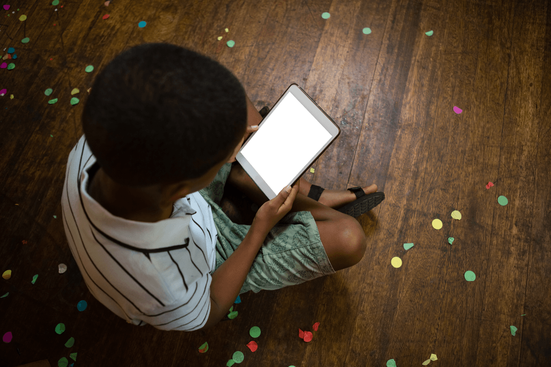 Boy Using Transparent Tablet on Wooden Floor with Confetti