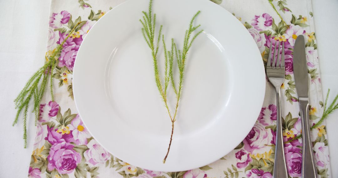 A white plate with a plant stem on a floral cloth hints at a spring meal or festive event. - Free Images, Stock Photos and Pictures on Pikwizard.com