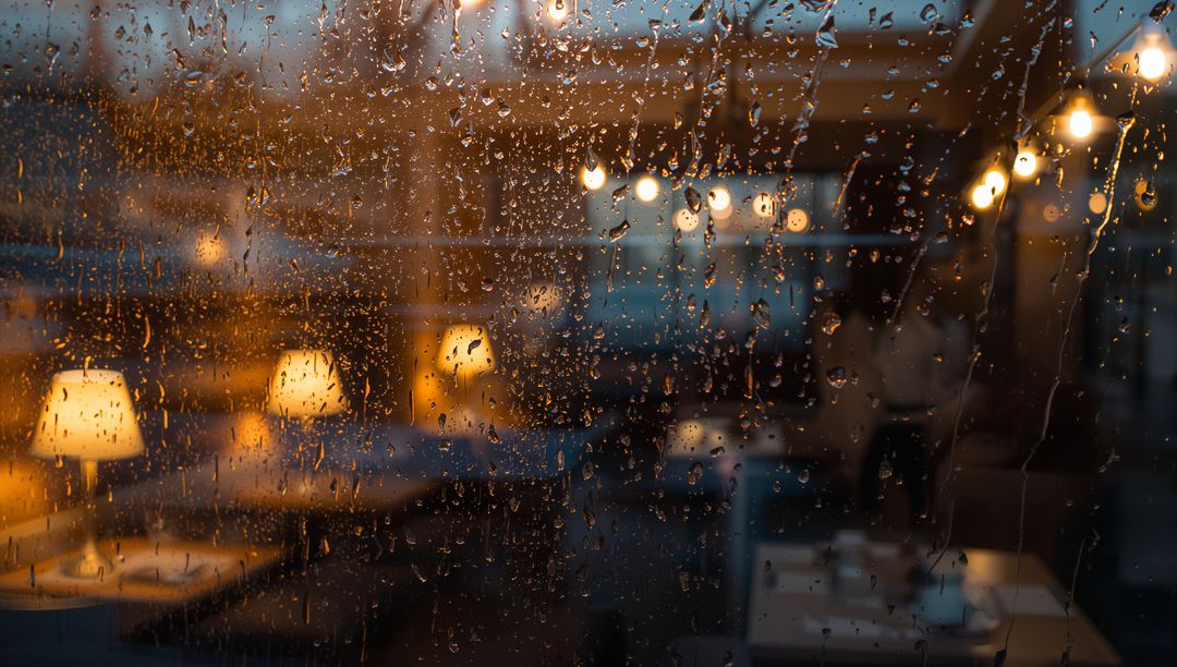 Raindrops on Window Overlooking Cozy Café Interior at Dusk with Warm Amber Glow