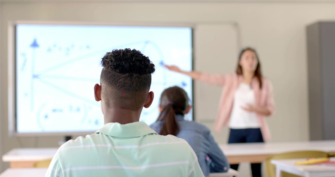 Teenagers watching teacher explaining graph on interactive display in modern classroom