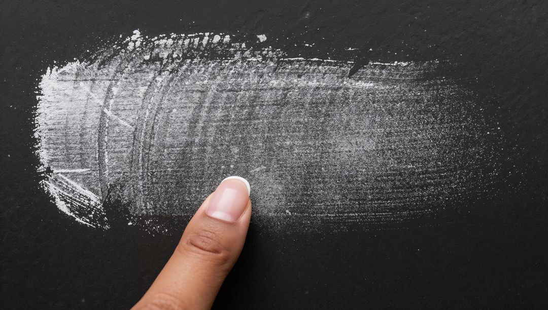 Index finger dragging white chalk smear on black slate surface closeup texture