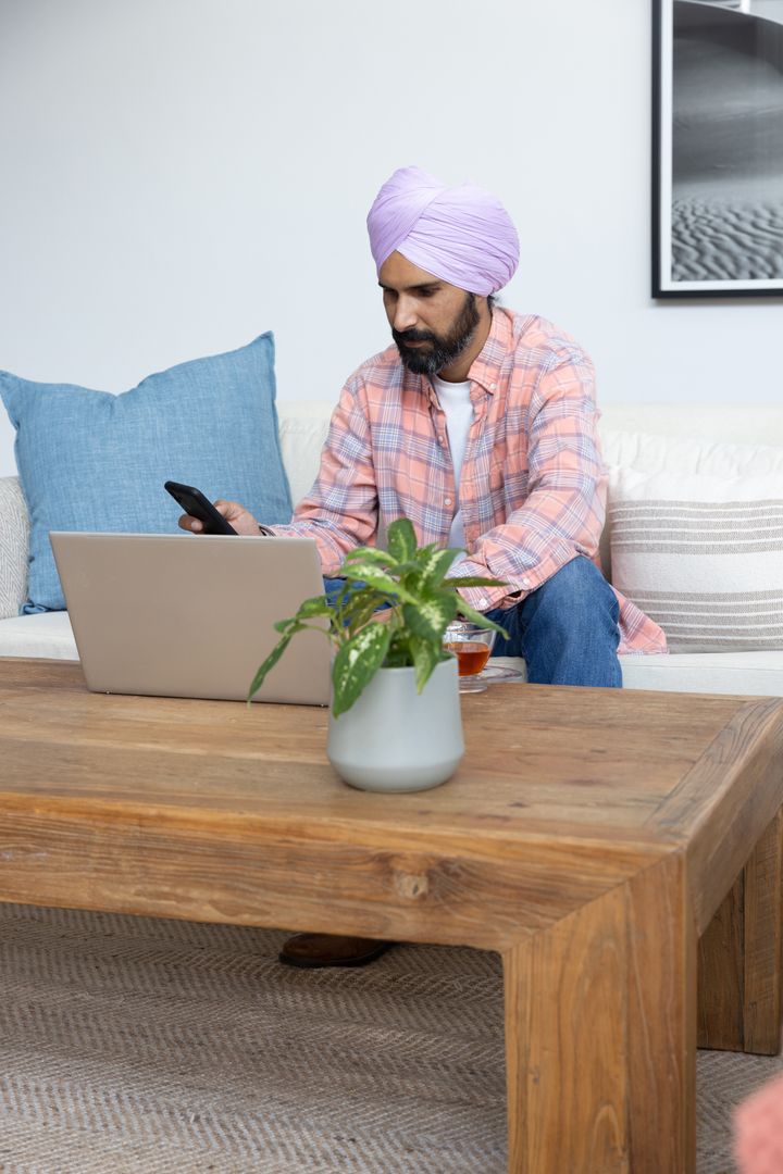 Mid Aged Indian Man Using Smartphone While Working on Laptop at Home