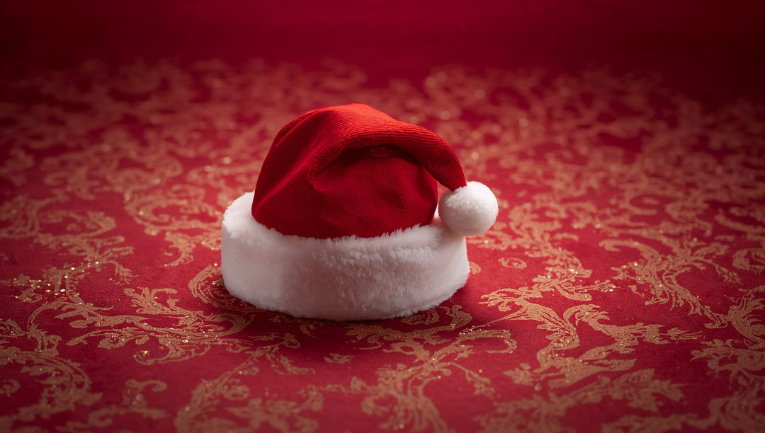 Santa hat resting on red and gold damask fabric featuring plush white brim and pom-pom