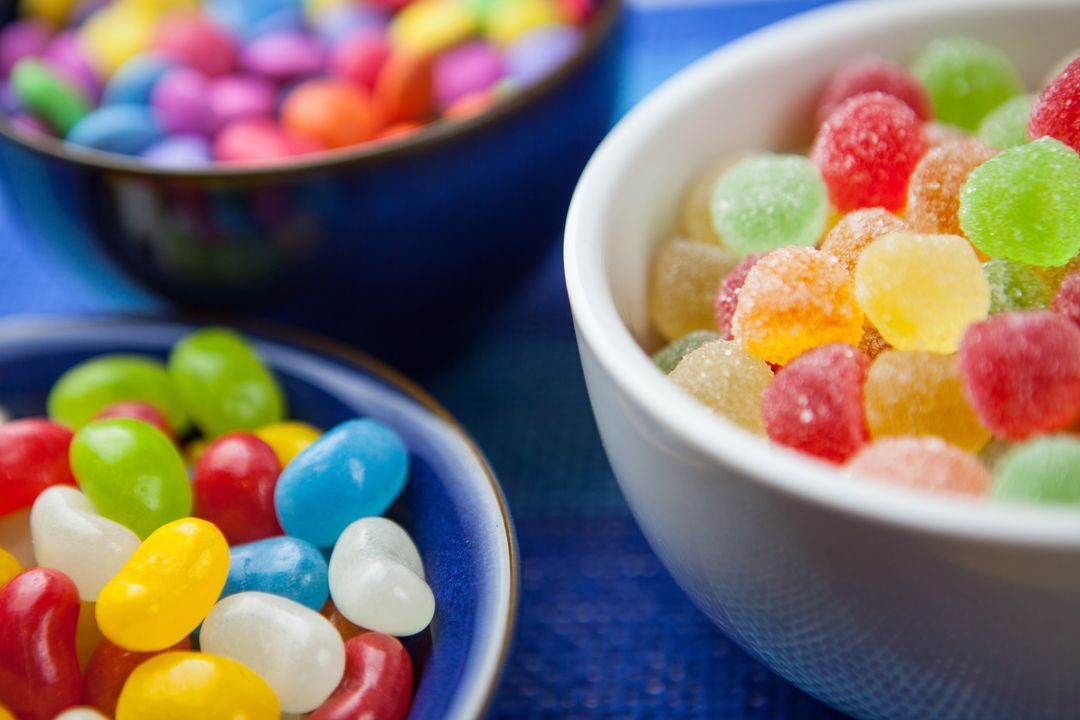 Displaying Colorful Jellybeans and Sugar-Coated Gumdrops in Bowls on Blue Surface