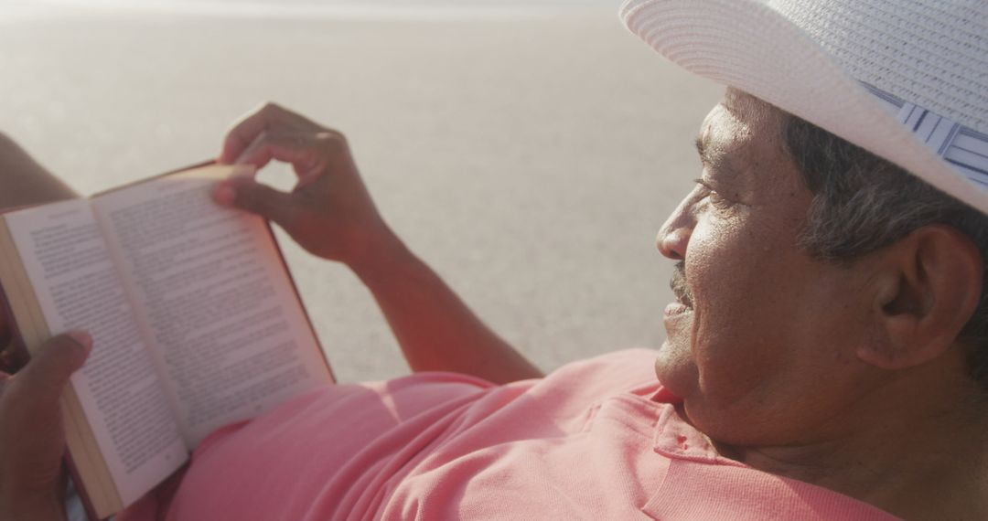 Senior Hispanic Man Relaxing on Beach Reading Book