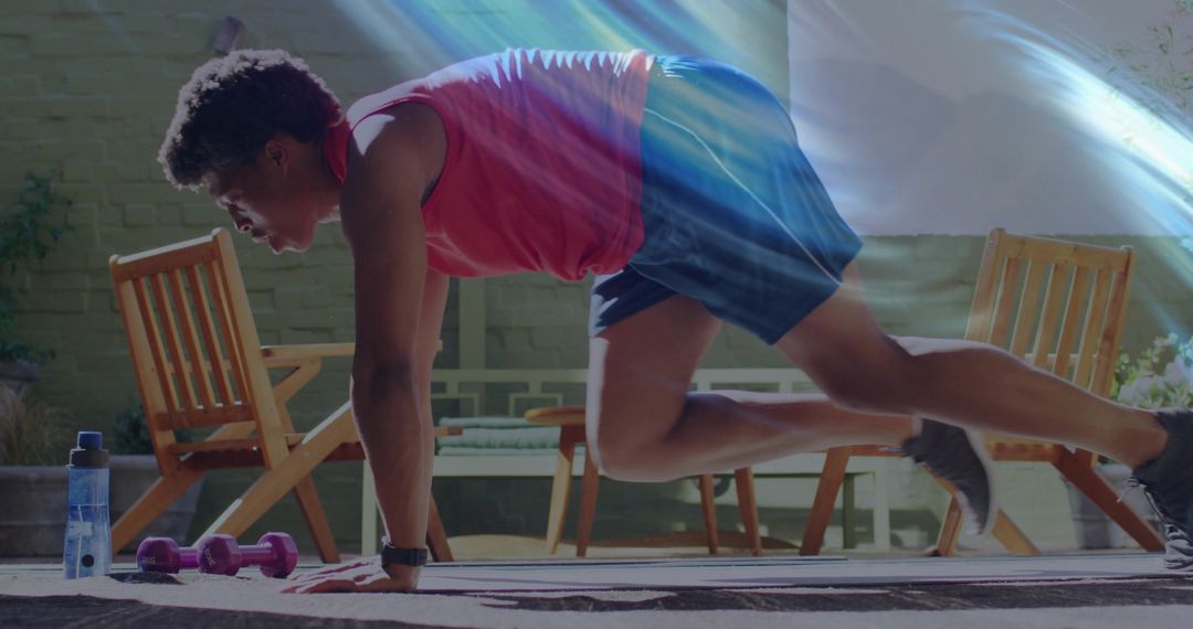 Man performing mountain climber exercise on backyard patio with dumbbells and water bottle