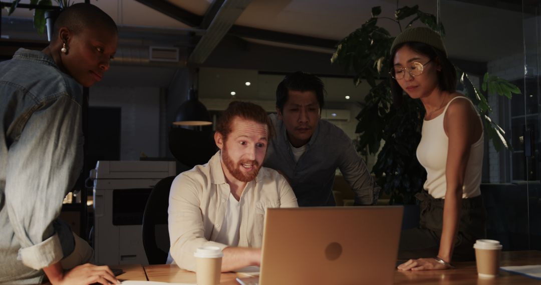 Diverse Team Collaborating on Laptop in Office at Night