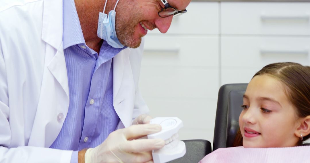 Smiling Dentist Showing Teeth Model to Young Girl Patient - Free Images, Stock Photos and Pictures on Pikwizard.com