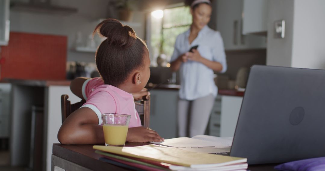 African American Girl Doing Homework While Mother is on Smartphone in Kitchen - Free Images, Stock Photos and Pictures on Pikwizard.com