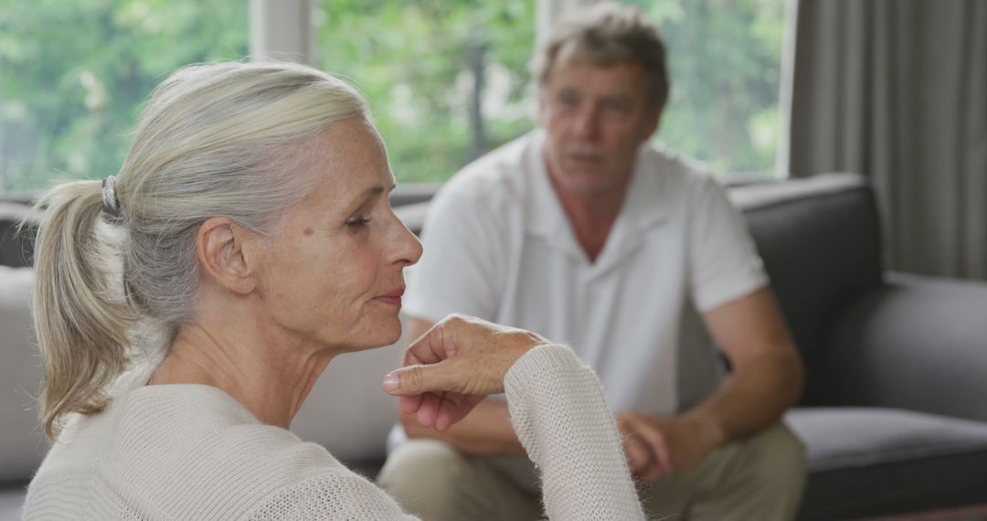 Thoughtful Senior Woman Sitting on Couch with Older Man in Background - Free Images, Stock Photos and Pictures on Pikwizard.com