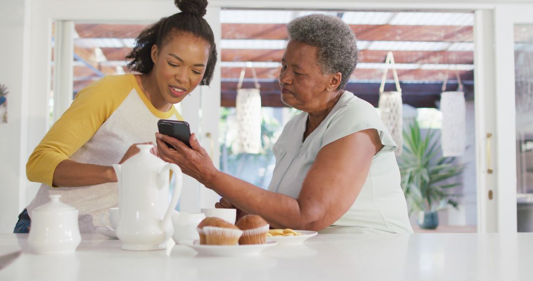 Young Woman Assisting Senior with Smartphone During Breakfast - Free Images, Stock Photos and Pictures on Pikwizard.com