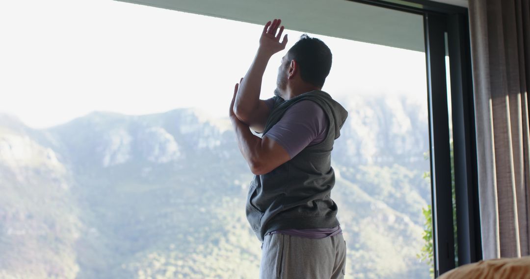Man Stretching by Window Overlooking Mountain View in Casual Attire