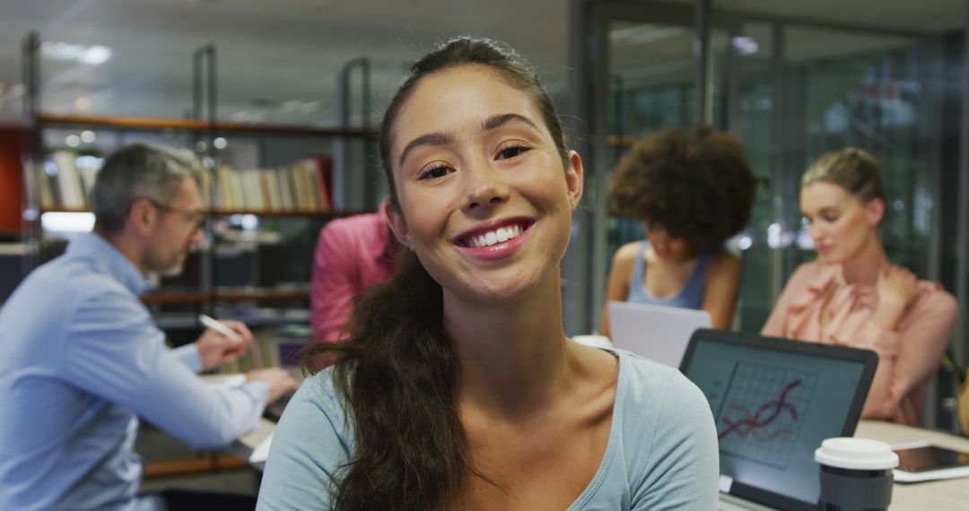 Smiling Woman in Office with Colleagues Working in Background - Free Images, Stock Photos and Pictures on Pikwizard.com