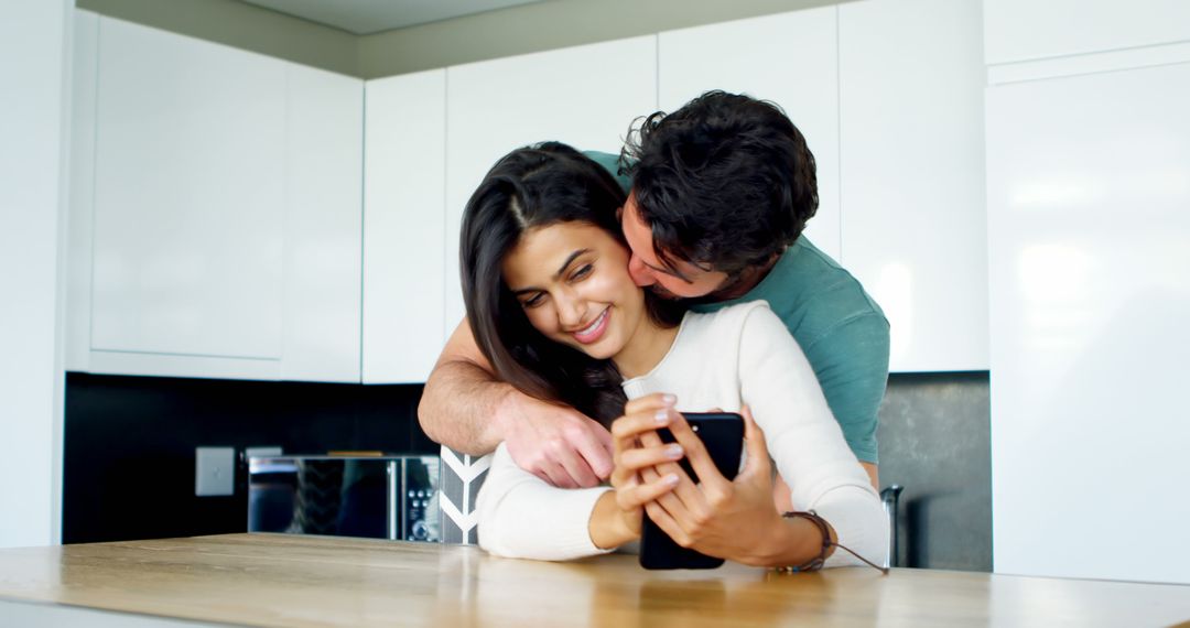 Joyful Couple Embracing While Sharing Moment on Smartphone in Modern Kitchen