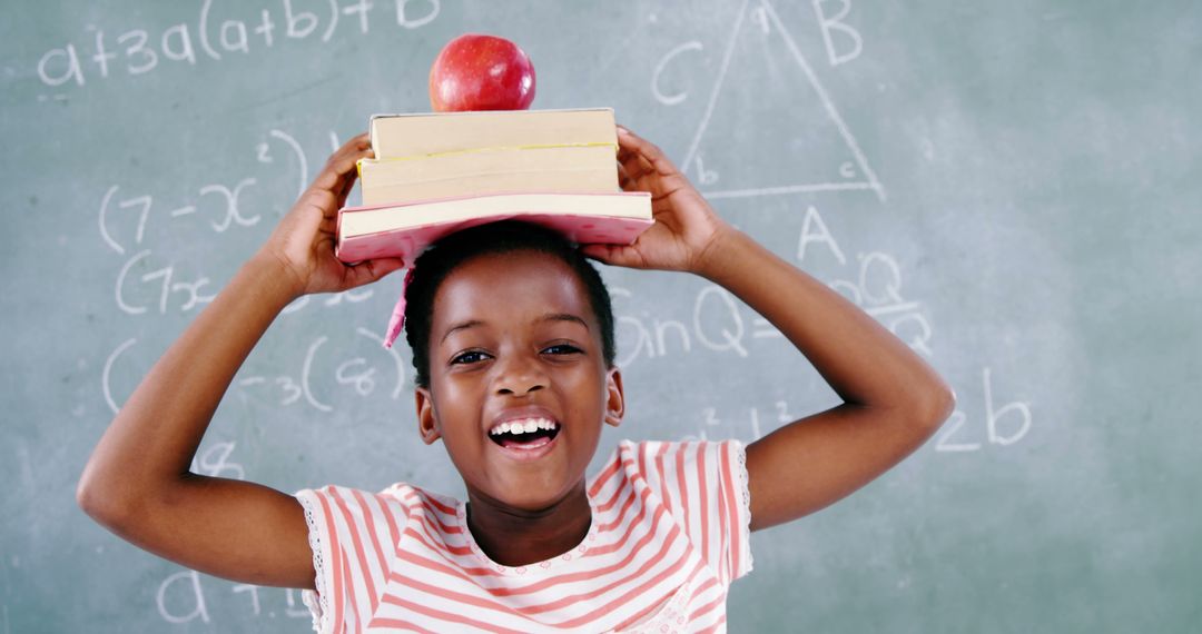 A girl exemplifies fun learning by balancing books and an apple while smiling at math equations. - Free Images, Stock Photos and Pictures on Pikwizard.com