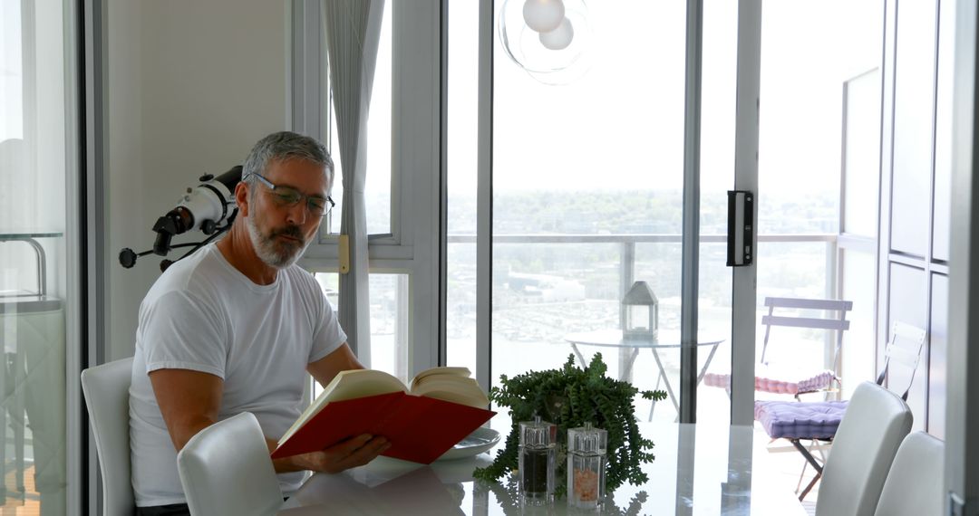 Senior Man Reading Book in Modern Apartment Dining Room - Free Images, Stock Photos and Pictures on Pikwizard.com