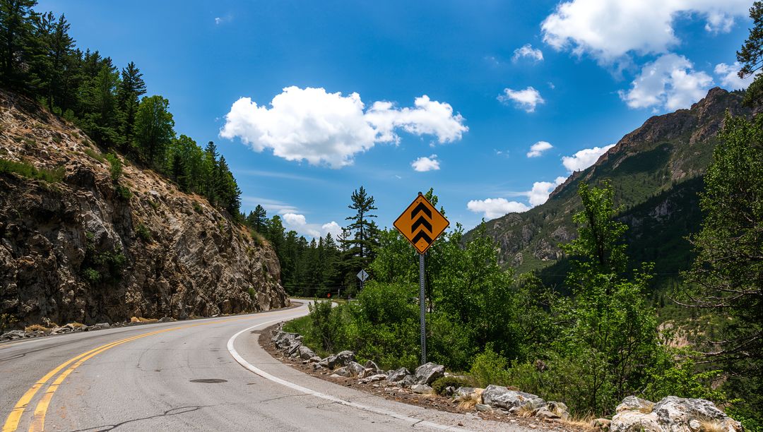 Winding mountain road curving through rocky pass with forested cliffs and blue sky
