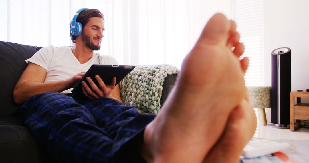 Man Relaxing on Couch with Tablet and Headphones - Free Images, Stock Photos and Pictures on Pikwizard.com